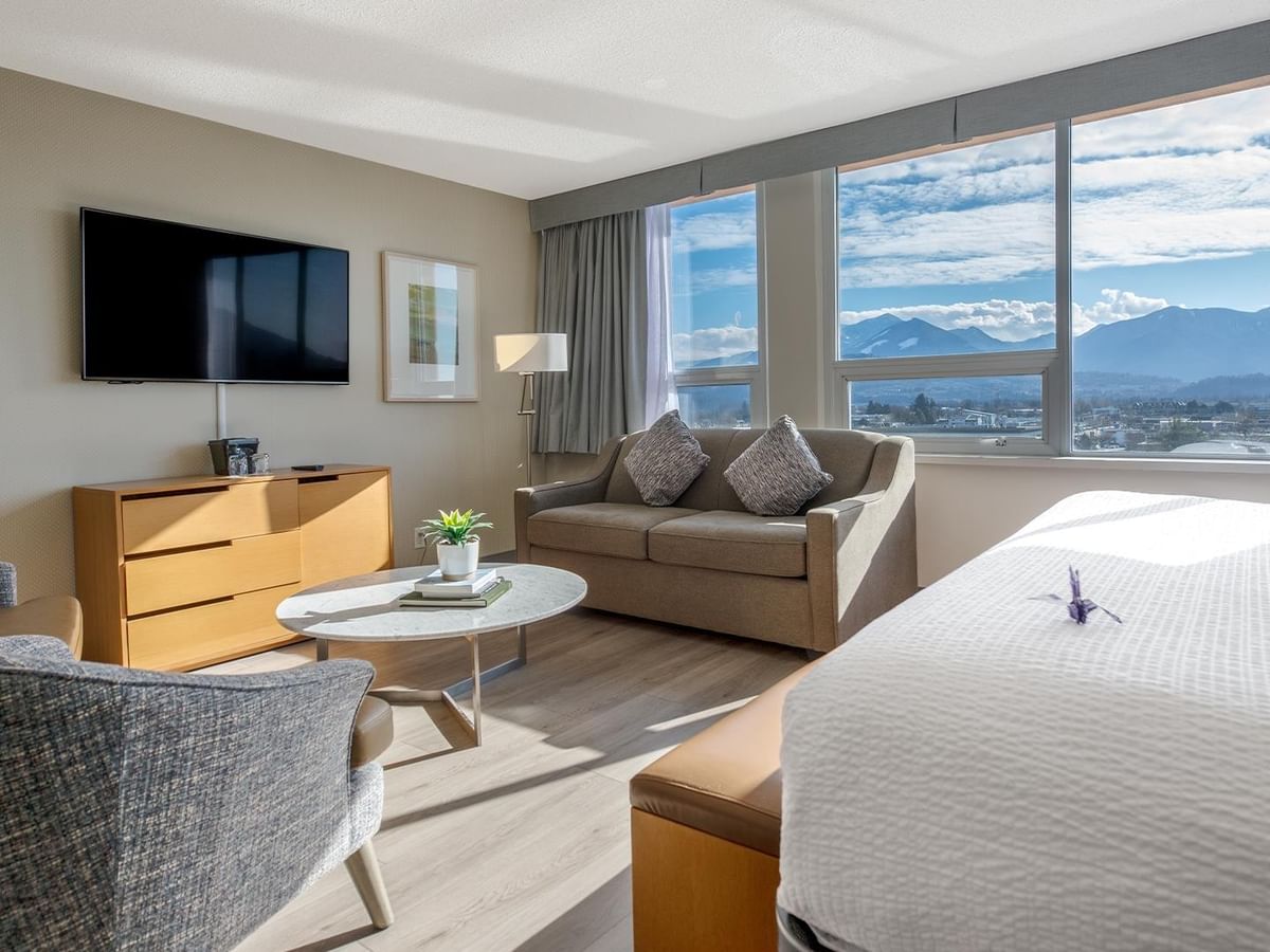 King bed, sofa, TV, and a large window with views at Coast Chilliwack Hotel by APA.