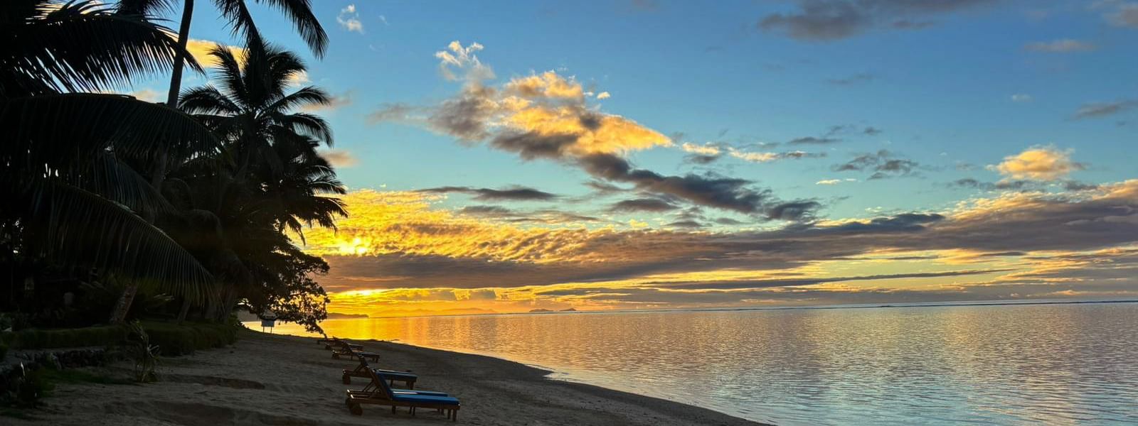 Sunset over the sand beach with lounge chairs at Warwick Fiji Resort and Spa in Korolevu