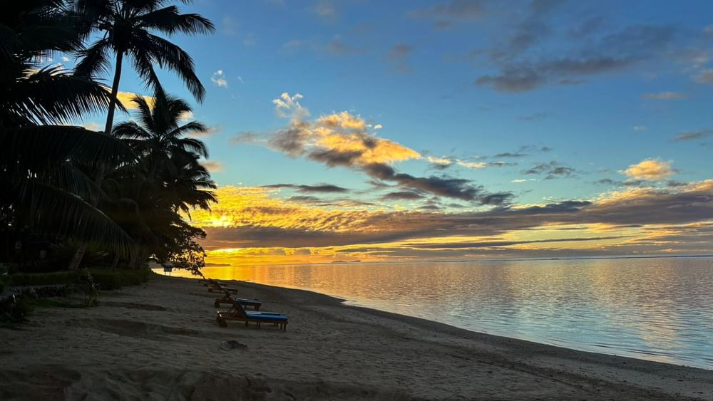 Sunset over the sand beach with lounge chairs at Warwick Fiji Resort and Spa in Korolevu.