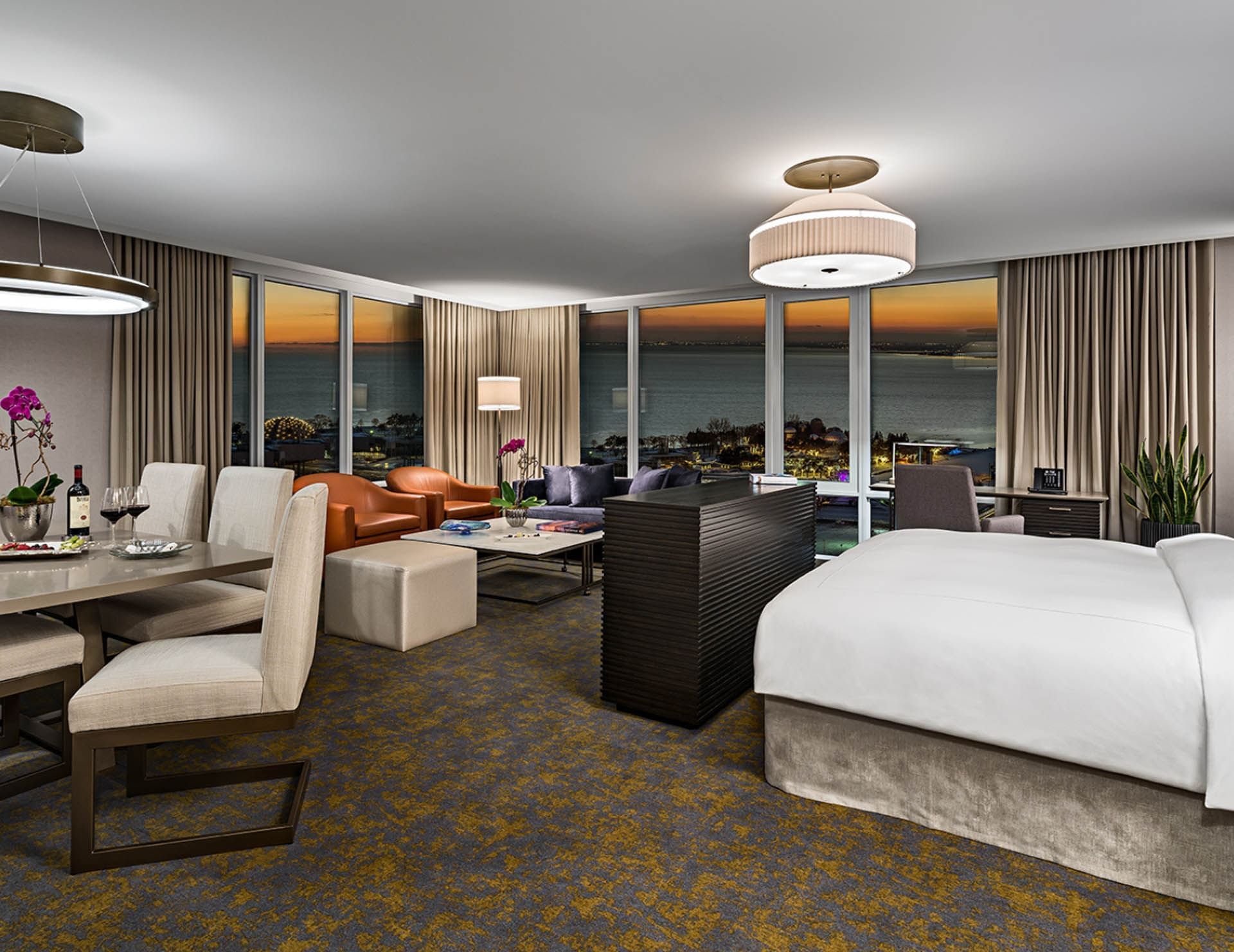 Modern suite with king bed and dining area facing floor to ceiling windows with sunset view over lake at Hotel X Toronto