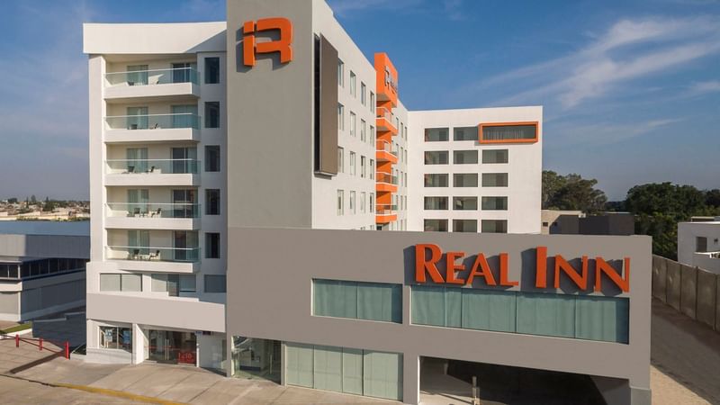 Real Inn Celaya hotel exterior under a blue sky, showcasing modern architecture with bold orange accents