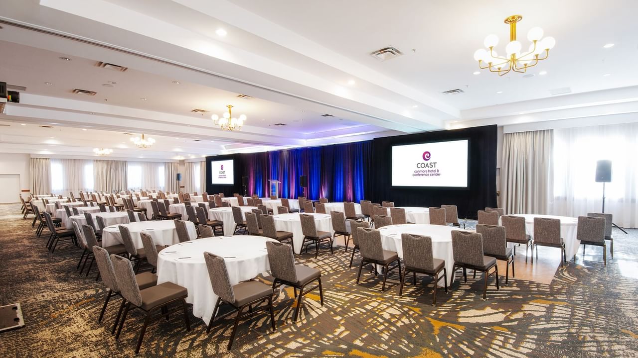 Large conference room with tables and chairs, two screens, and a podium.