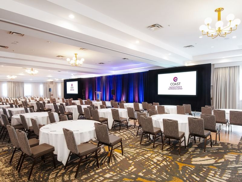 Large conference room with tables and chairs, two screens, and a podium.