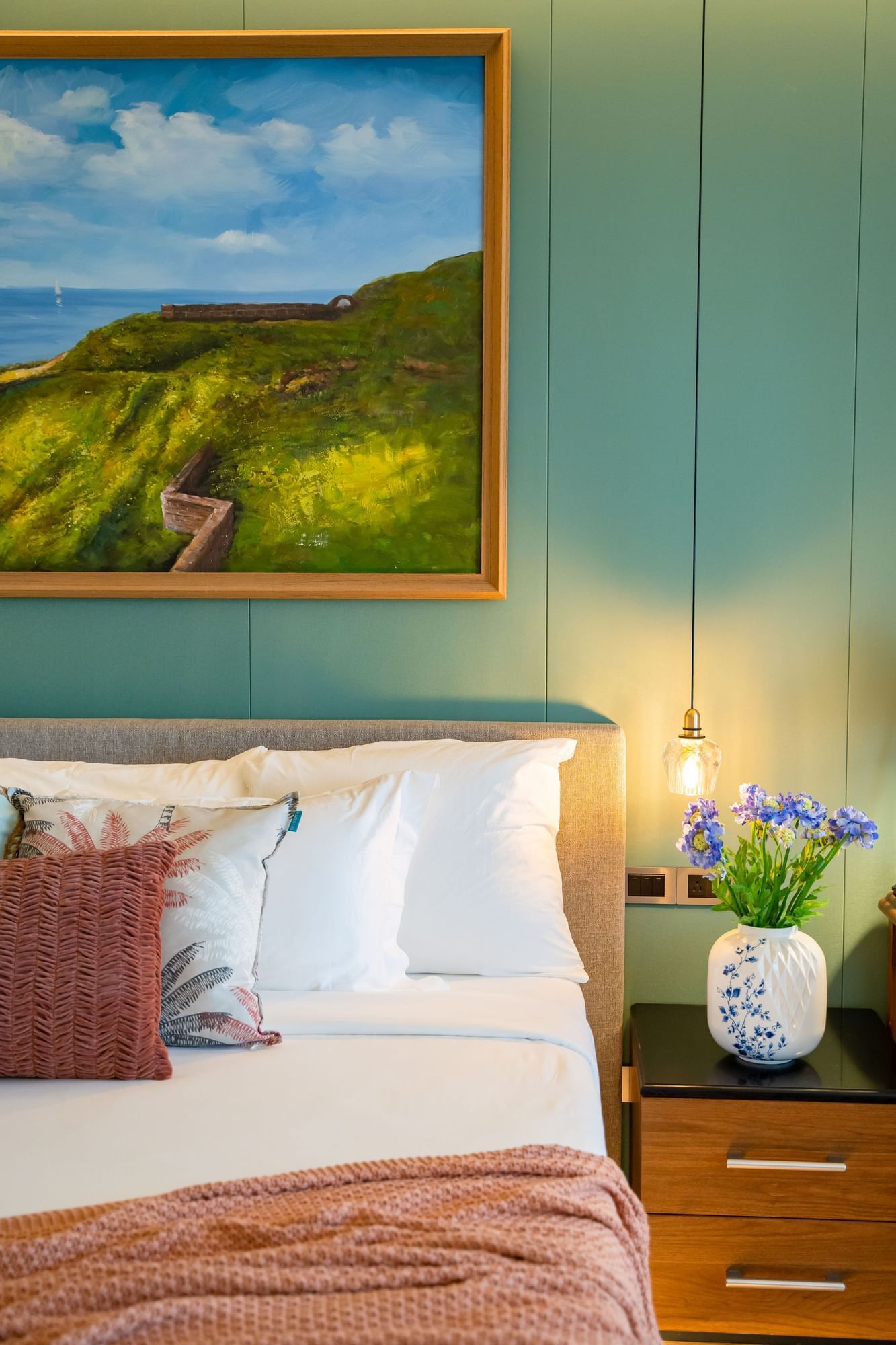 Deluxe Ocean View Room met zacht bed en vaas met blauwe bloemen verlicht door hanglamp bij Golden Rock Resort