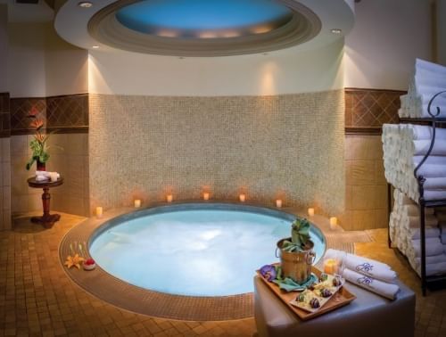 A small indoor whirlpool beneath a skylight surrounded by candles, a towel rack, and a tray with Champagne and chocolate covered strawberries.