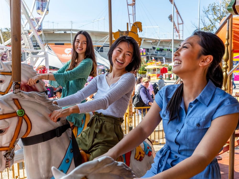 Three women smiling and riding horses on a merry-go-round at Sydney Royal Easter Show 2026.