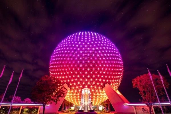 Spaceship Earth at EPCOT illuminated at night and glowing pink, red, and orange.