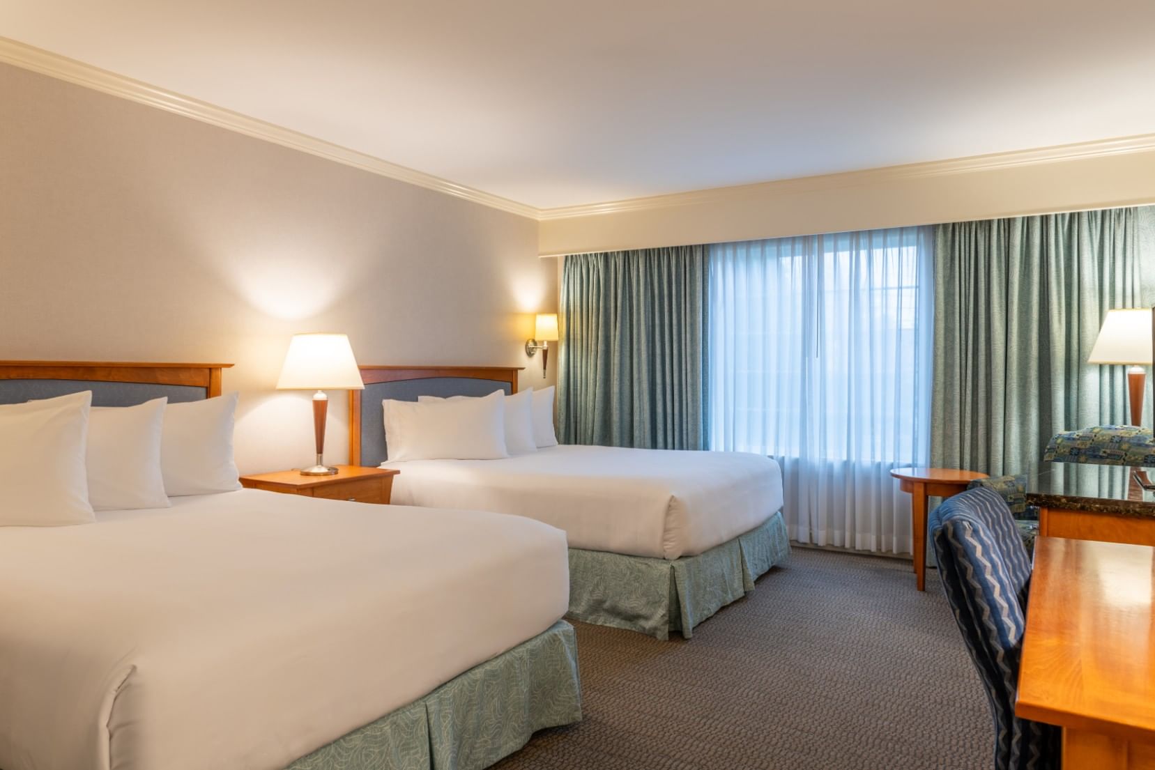 A hotel room with two queen beds, a desk, and a window with curtains.