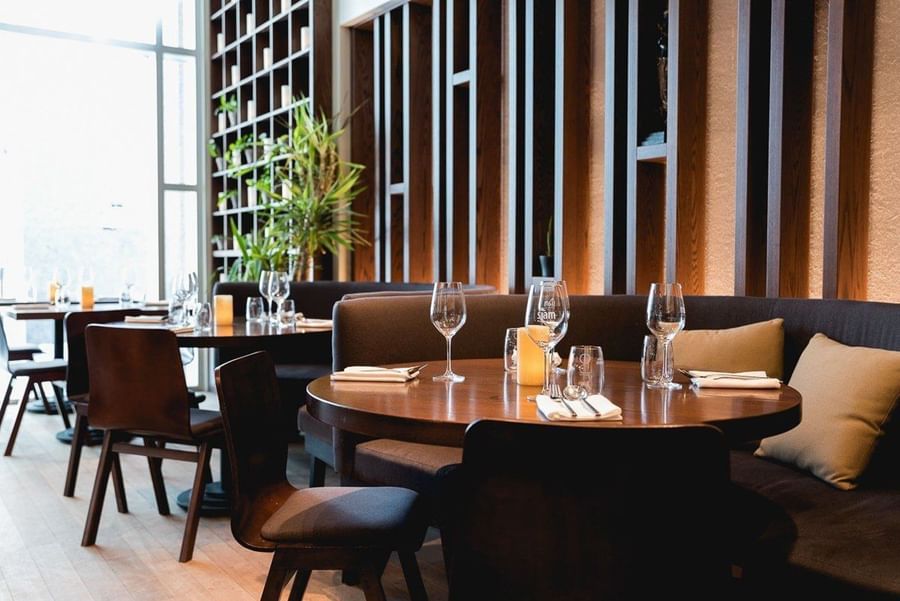 Dining tables with wine glasses by sofas under wooden wall slats in Siam Downtown Montreal at Warwick Le Crystal Montreal