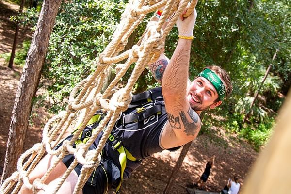 Person in harness climbing a rope at Tree Trek Adventure Park near Lake Buena Vista Resort Village & Spa