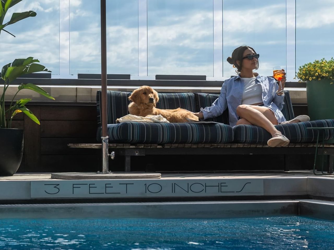 Woman lounging with a drink beside her dog on striped pool seating at Gansevoort Meatpacking NYC