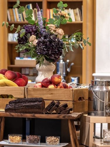 Table with fresh fruit, sliced chocolate cake, and a cereal station in the Roseraie Room at Warwick Reine Astrid - Lyon