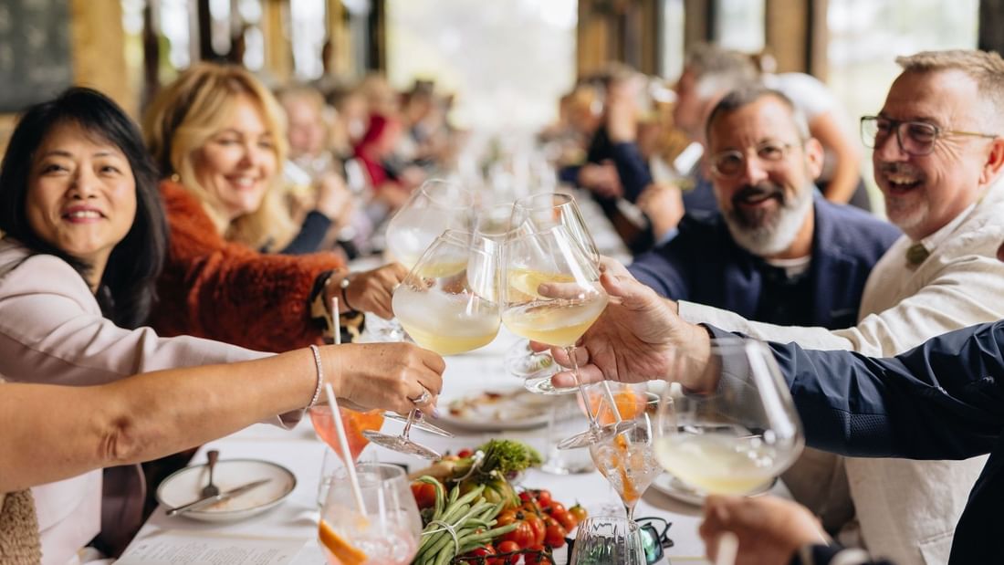 Guests toasting with wine glasses at a communal dining table featuring fresh food and vibrant conversation