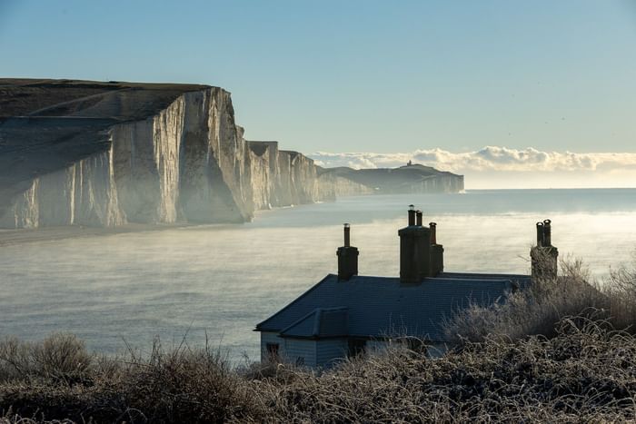 House with three chimneys in front of Seven Sisters cliffs and sea in the morning.