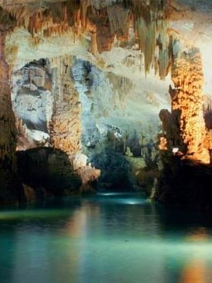 Jeita Grotto, featuring lit rock columns by calm water under stone ceilings near Warwick Palm Beach Hotel