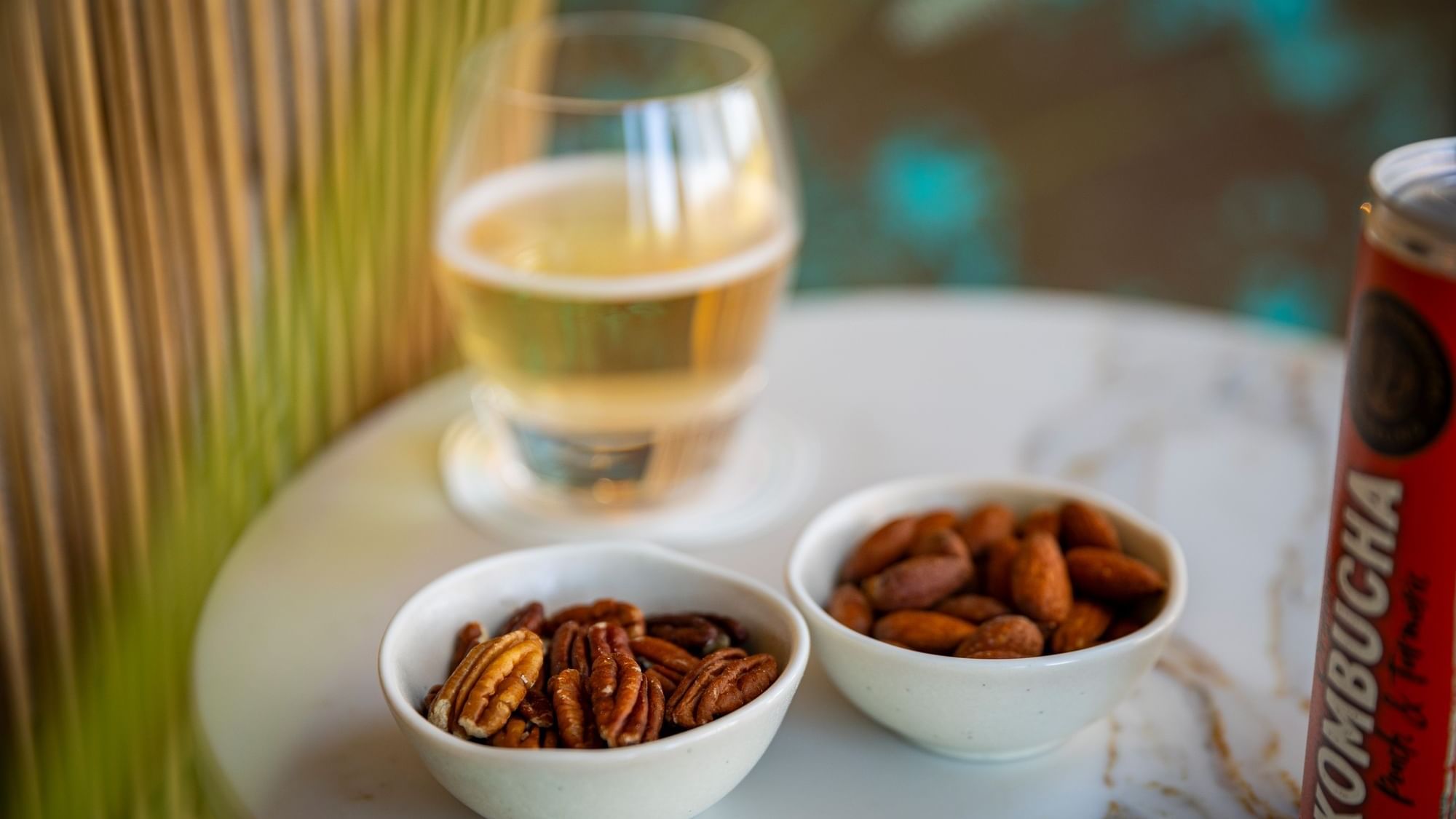 Snack bowls of roasted almonds and pecans next to a glass of sparkling cider and a kombucha can at Dunluce Lodge