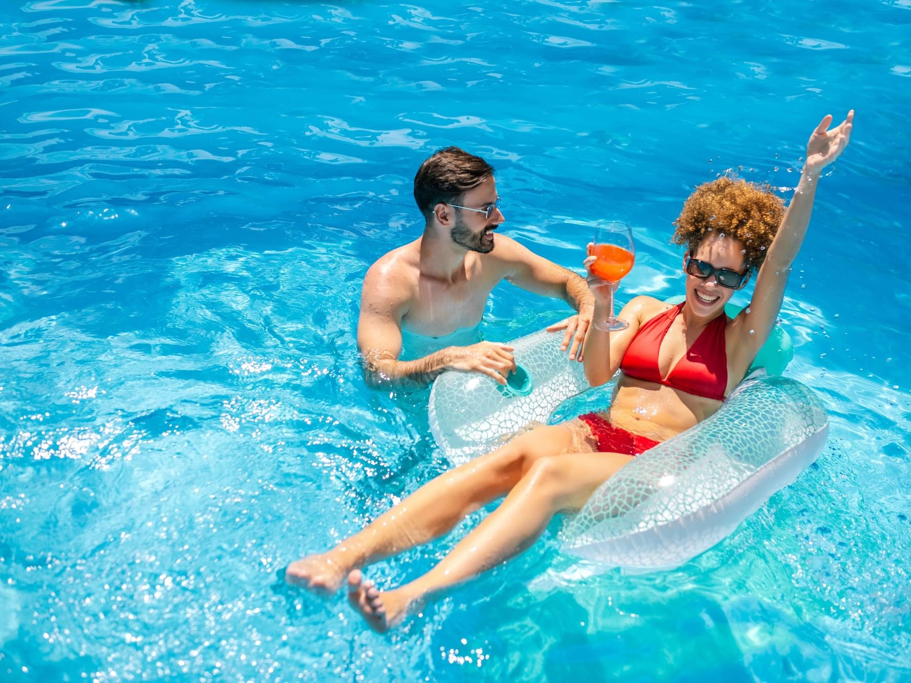 Couple relaxing in a pool with floaters and drinks for a Romantic Getaway.