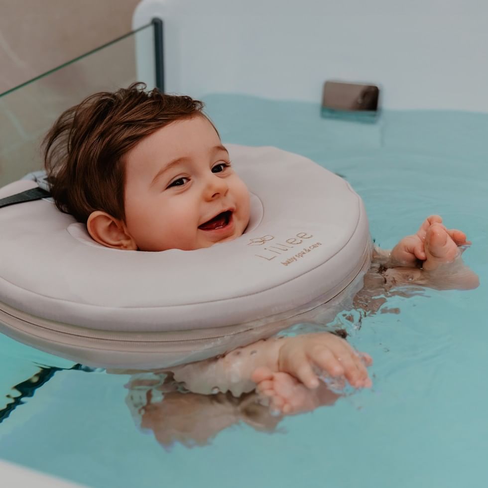 Lachendes Baby mit Schwimmhilfe im türkisfarbenen Wasser beim Lillee Mama & Baby Retreat