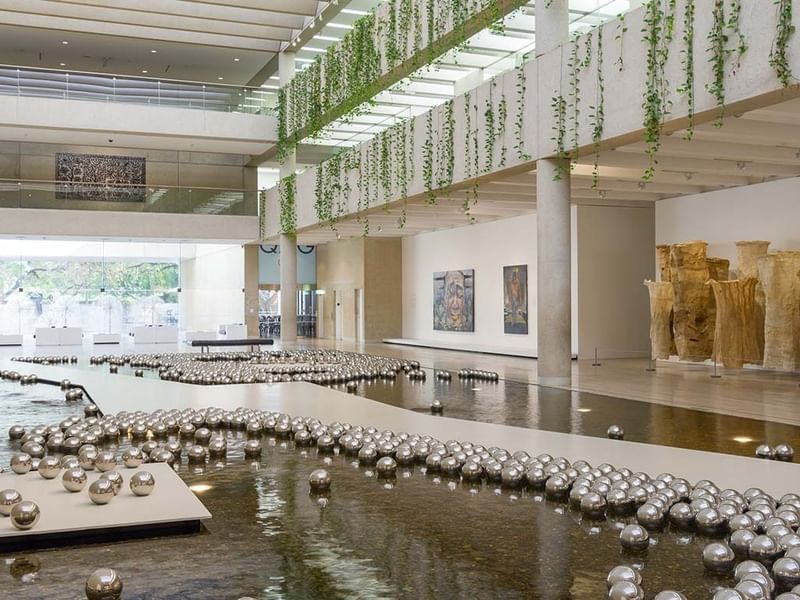 Modern art gallery interior with reflective water feature, hanging greenery, and contemporary sculptures at QAGOMA