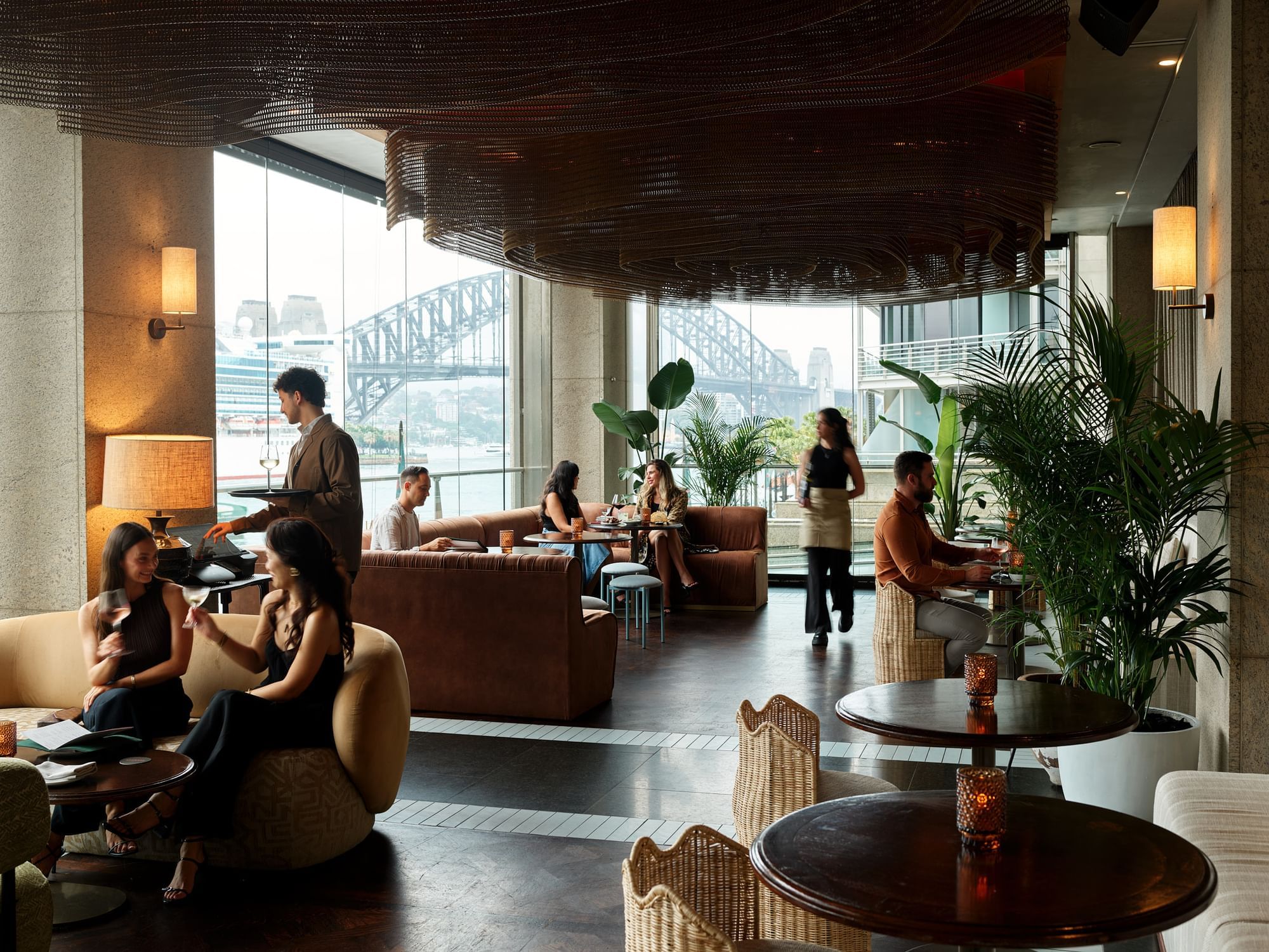 People lounging and dining in a restaurant overlooking the Sydney Harbour Bridge at Pullman Quay Grand Sydney