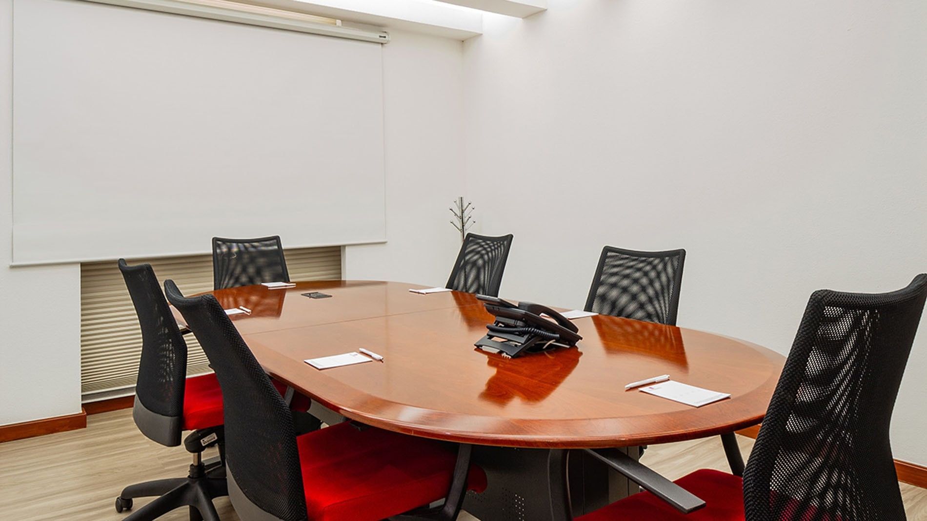 Small meeting room featuring a wooden oval table with red-seated chairs at Camino Real Aeropuerto Mexico