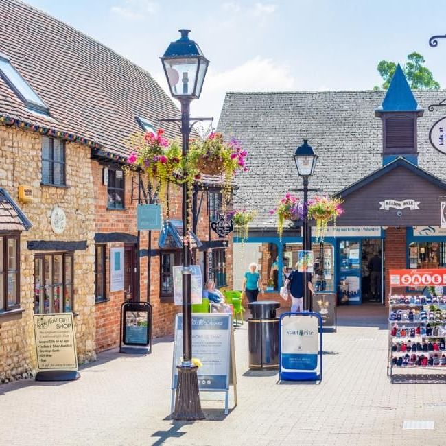 Charming pedestrian shopping street with historic stone buildings, hanging baskets, and traditional street lamps in Buckingham.