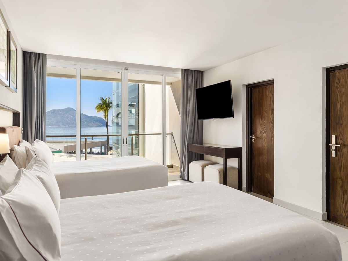 Deluxe room with two white beds, a wall-mounted TV, and a scenic ocean balcony view at Sunvivia Mazatlán