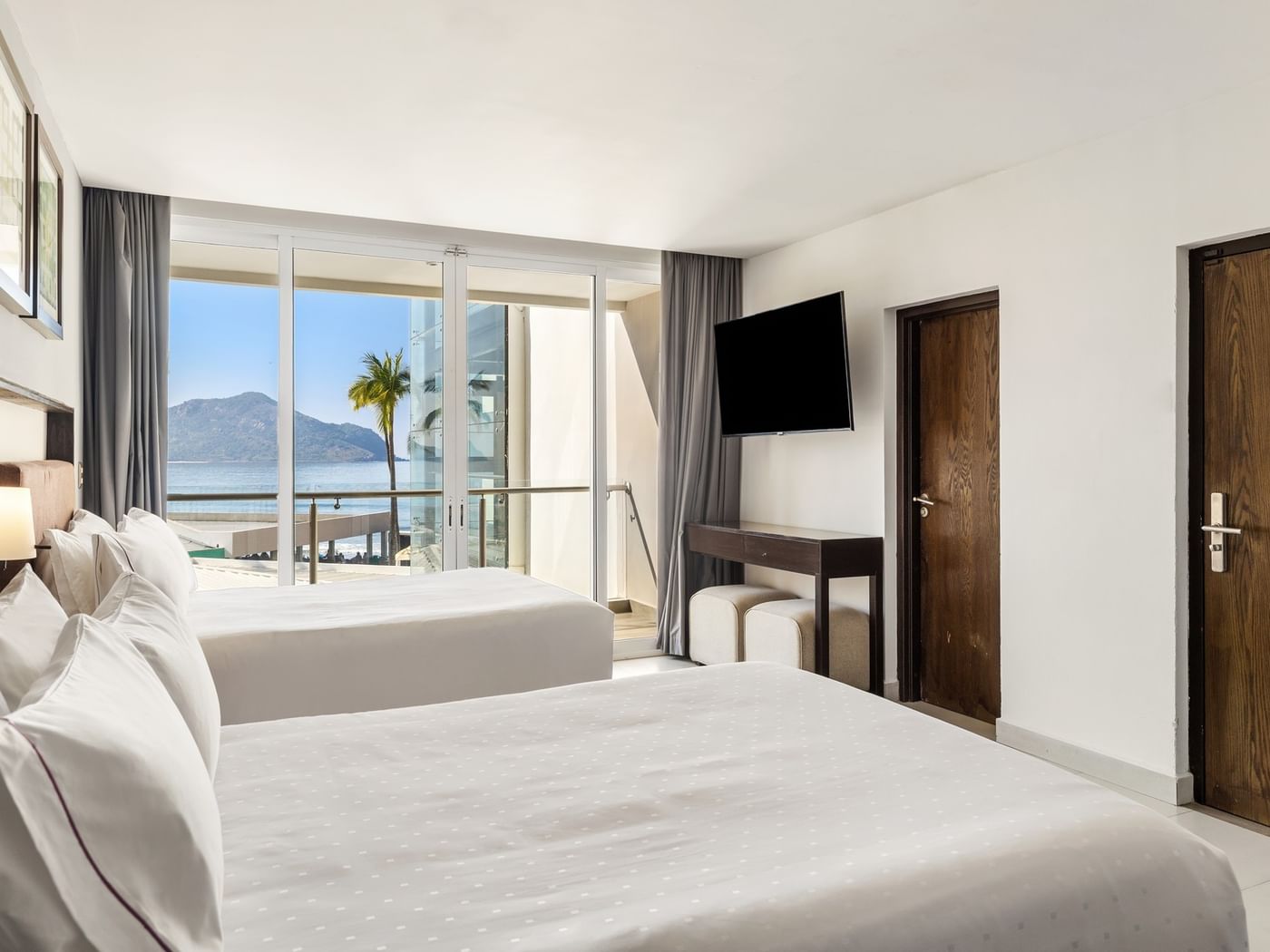 Deluxe room with two white beds, a wall-mounted TV, and a scenic ocean balcony view at Sunvivia Mazatlán