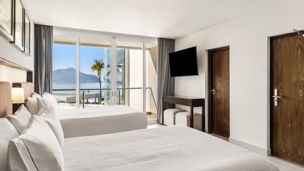 Deluxe room with two white beds, a wall-mounted TV, and a scenic ocean balcony view at Sunvivia Mazatlán