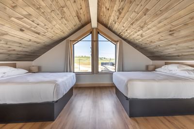 Cozy attic-style bedroom with two beds, wooden ceiling, and large windows in the Villa at Off Shore Resort