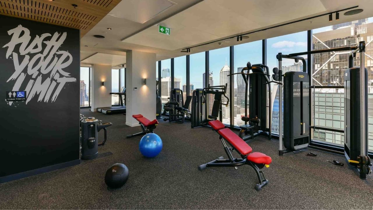 Modern gym with large windows, free weights, machines, and motivational wall text.