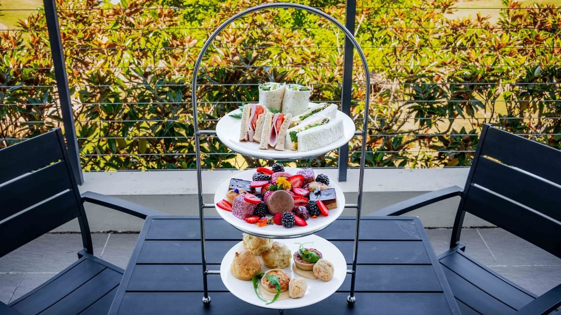 Three-tiered afternoon High Tea set on a table with a garden view in the background at Mercure Kooindah Waters