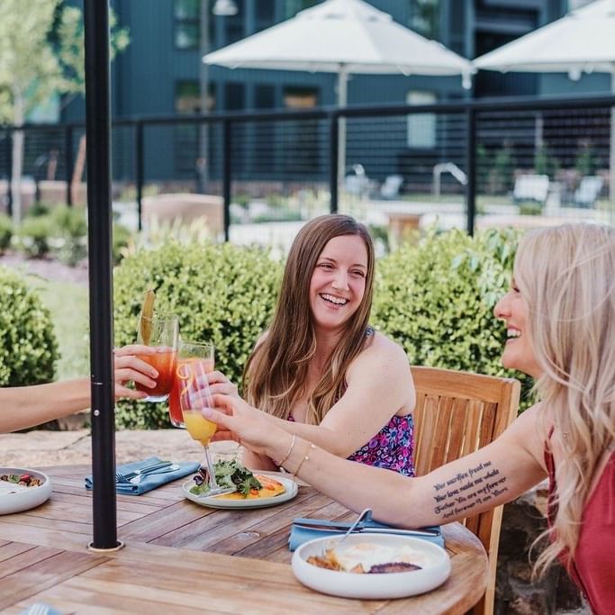 Three women toasting drinks at an outdoor table at The Porch Social.