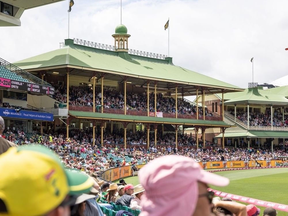 Crowded cricket stadium with distinctive green-roofed pavilions filled with spectators during Men's T20I Series match