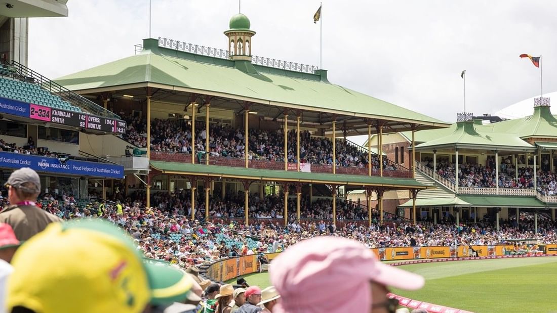 Crowded cricket stadium with distinctive green-roofed pavilions filled with spectators during Men's T20I Series match
