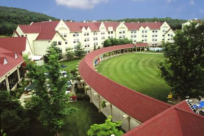 Aerial view of a large Branson Hillside Hotel complex with red roofs and a curved covered walkway on a sunny day