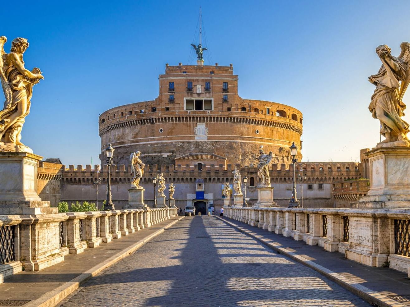 Castel Sant'Angelo framed by statues and a cobblestone path under a clear blue sky near The Guardian Hotel