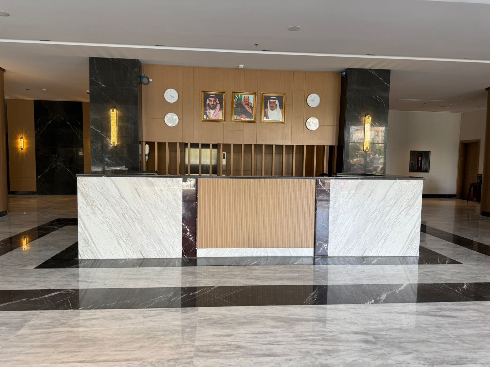 Marble reception desk by dark pillars under wall-mounted clocks in the lobby at Warwick Jeddah Hotel & Spa