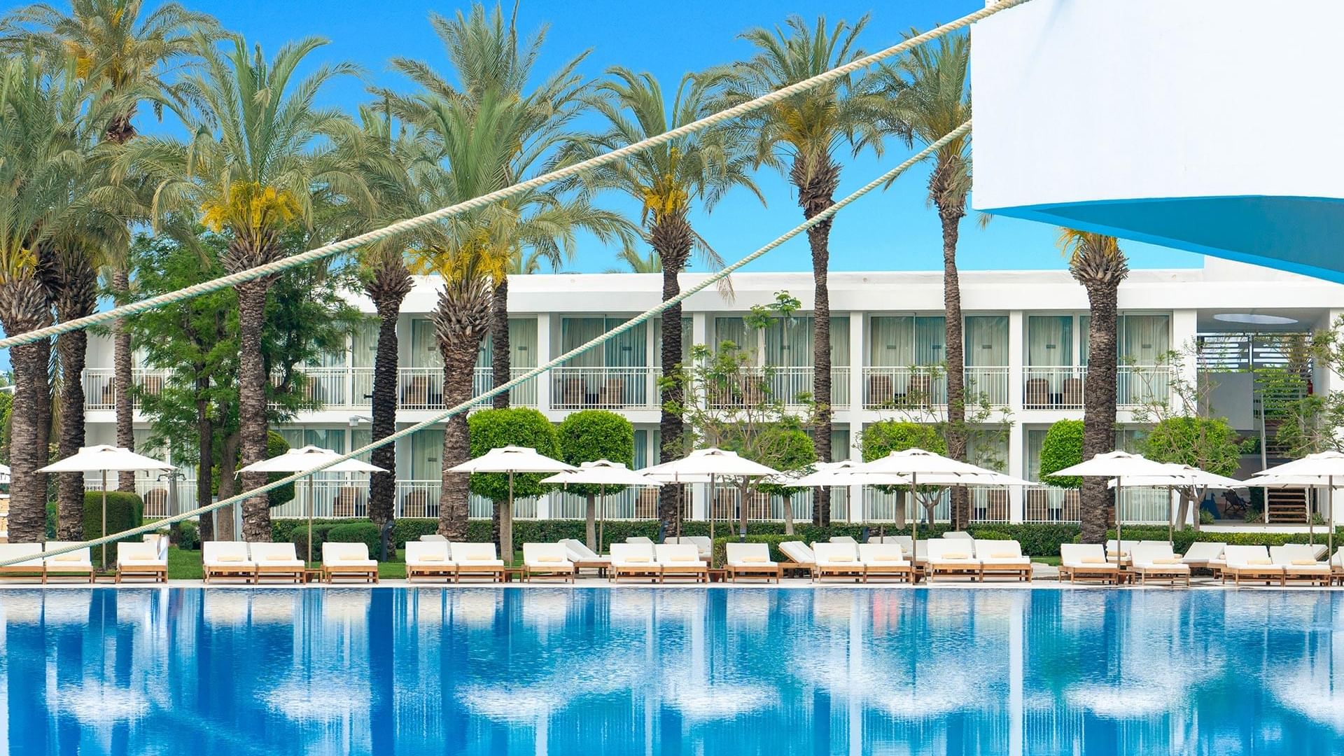 Голубой бассейн в Titanic Deluxe Lara – Annex Family, окружённый пальмами и оснащённый шезлонгами.