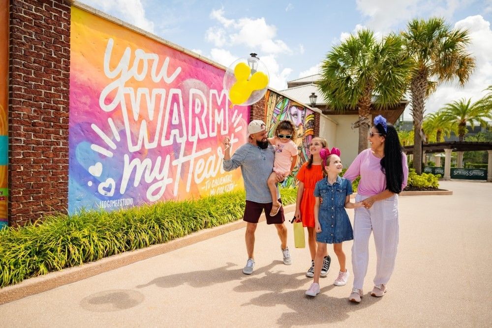 A mom, dad, and three daughters walk in front of a colorful mural at Disney Springs on a back-to-school weekend escape in Orlando.