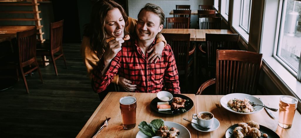 A person hugs their partner from behind in a restaurant while on a romantic weekend getaway in Canmore.