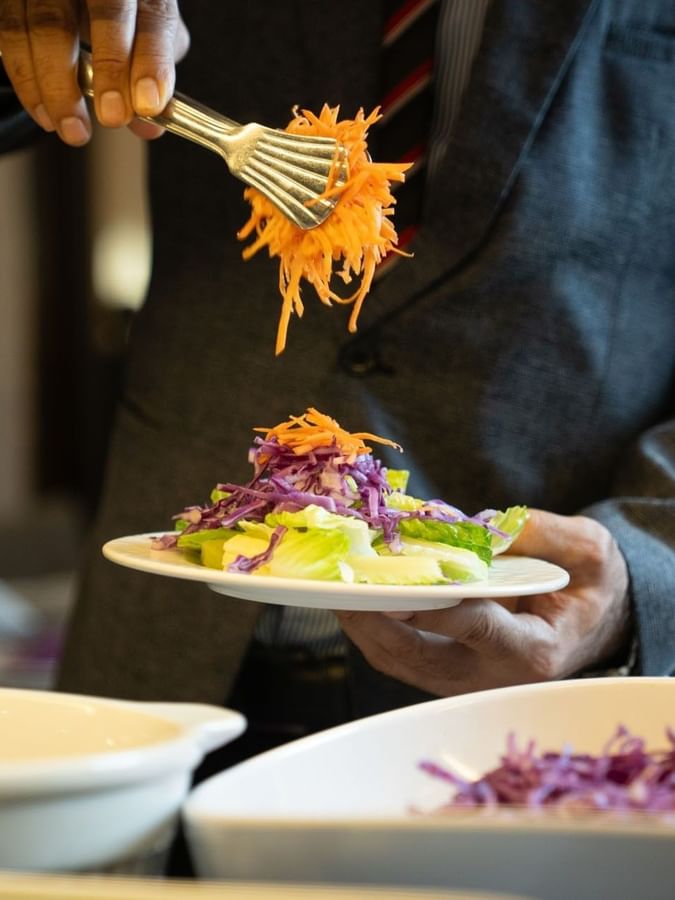 Person add shredded carrots to fresh salad in Al Firdous Restaurant at Saja Warwick Madinah