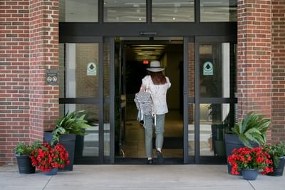 Rear view of a woman with a hat & striped backpack walking through the glass doors of the brick Rodd Grand Yarmouth building