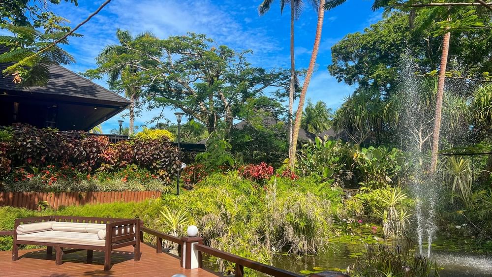 A serene wooden deck with a bench overlooking lush gardens and a fountain at The Naviti Resort in Korolevu.