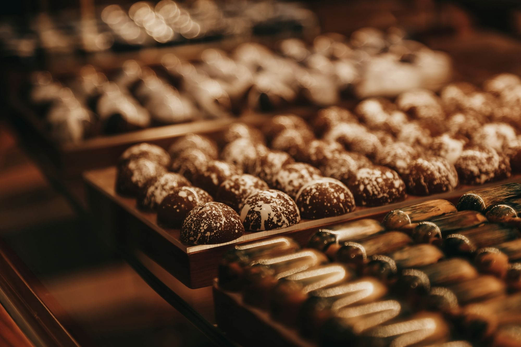A close-up of rows of assorted chocolate truffles with white speckles, arranged on a wooden tray.