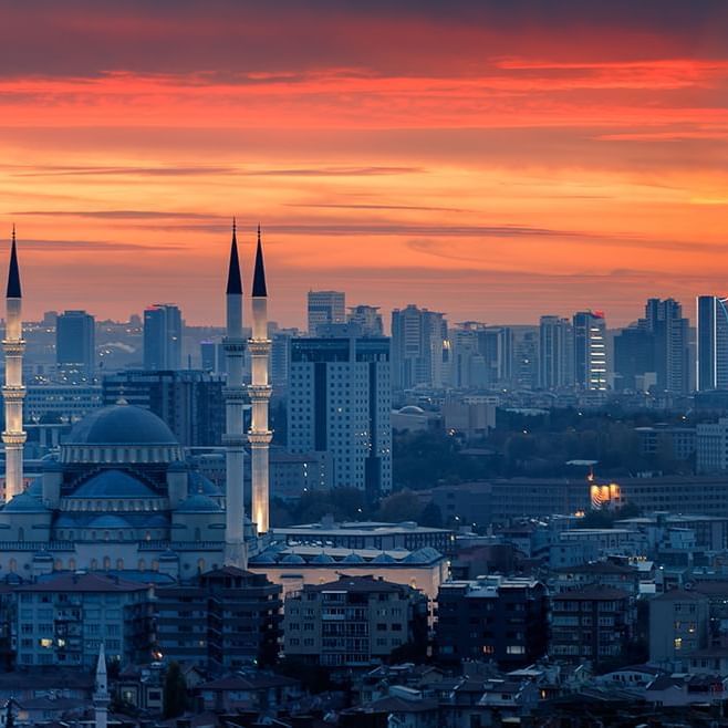 A panoramic view of a city at sunset, featuring a Ankara mosquee with tall minarets near Warwick Hotels and Resorts