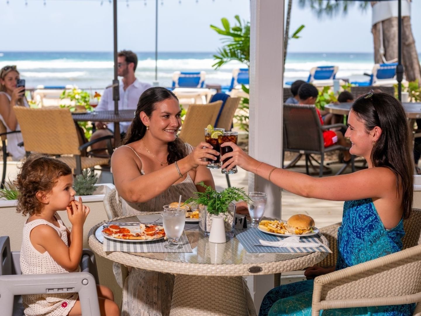 Two women and a child dining at an outdoor table with ocean view at Savannah Beach Hotel.