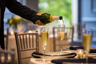 Server pouring champagne into a flute glass at an elegant banquet dinner table in Sable Oaks Weddings and Events