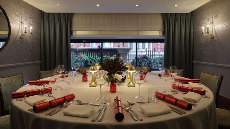 Round dining table set with red crackers and gold lamps by a window at Warwick Hotels & Resort