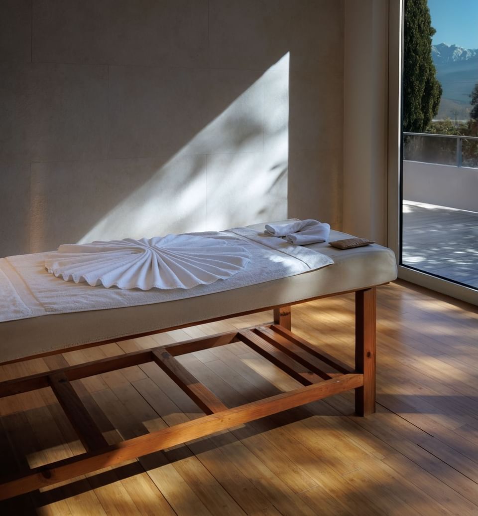 Spa room with sunlight on a massage bed, towel art, and mountain view through window at The Terraces Resort & Spa